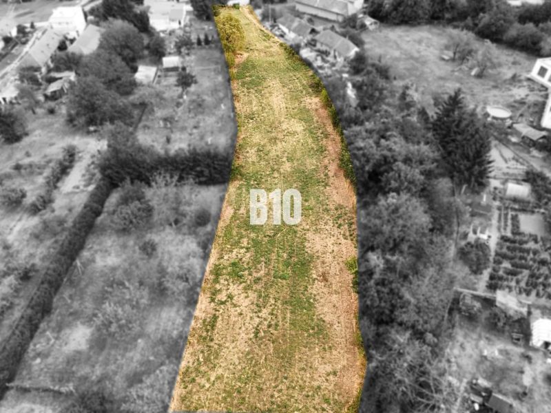 Na predaj pozemok v Kolíňanoch – 2 700 m² - Pozemky - bývanie Kolíňany: Dlhý pozemok so zelenou trávou, lemovaný stromami a stavbami.