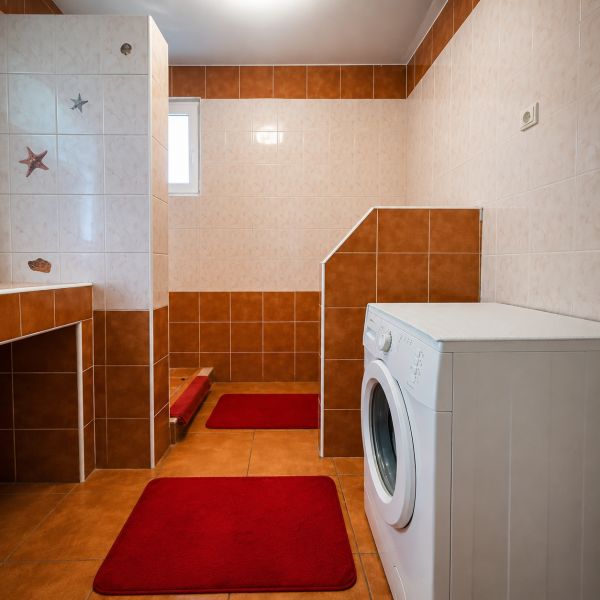 Na predaj zrekonštruovaný 4-izbový rodinný dom v Šalgočke  - Kúpeľňa v rodinnom dome so sprchovým kútom a práčkou, dlažba v odtieňoch hnedej.