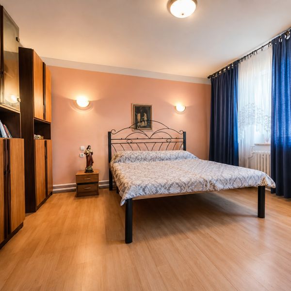 Na predaj zrekonštruovaný 4-izbový rodinný dom v Šalgočke  - Spálňa s kovovou posteľou, podlaha s dreveným dekorom, nábytok a závesy v rodinnom dome.