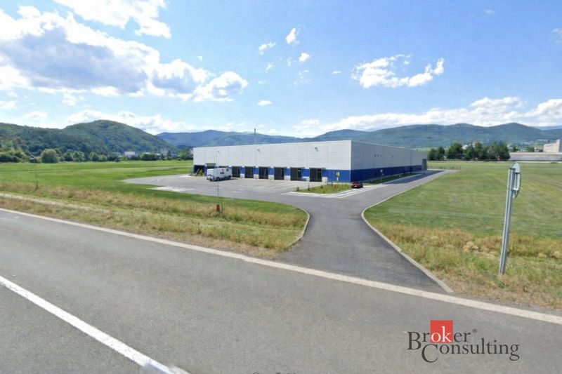 Investičná príležitosť: Komerčný pozemok 8 861 m² s platnou ÚPI v Hlin - Komerčné pozemky v Hliníku nad Hronom s priemyselnou halou, obklopené kopcovitou krajinou.