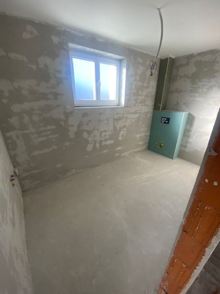 Ponúkame na predaj Rodinný dom v Rovinke na Platanovej ulici - Nedokončená miestnosť v rodinnom dome s oknom a zeleným nástenným prvkom.