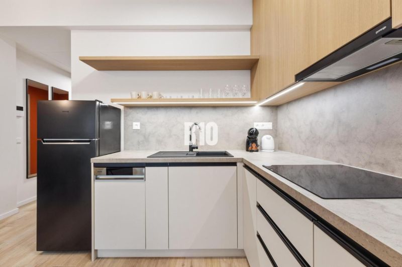 DOWNTOWN NA DOSAH – DIZAJNOVÝ 1-izbový apartmán s loggiou a výhľadom n - Kuchyňa v 1-izbovom byte s podlahou s dreveným dekorom a čiernou chladničkou.