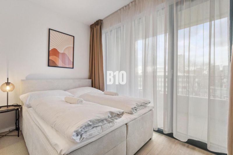 DOWNTOWN NA DOSAH – DIZAJNOVÝ 1-izbový apartmán s loggiou a výhľadom n - Spálňa s posteľou, nočným stolíkom, obrazom a priesvitnými závesmi v 1-izbovom byte.