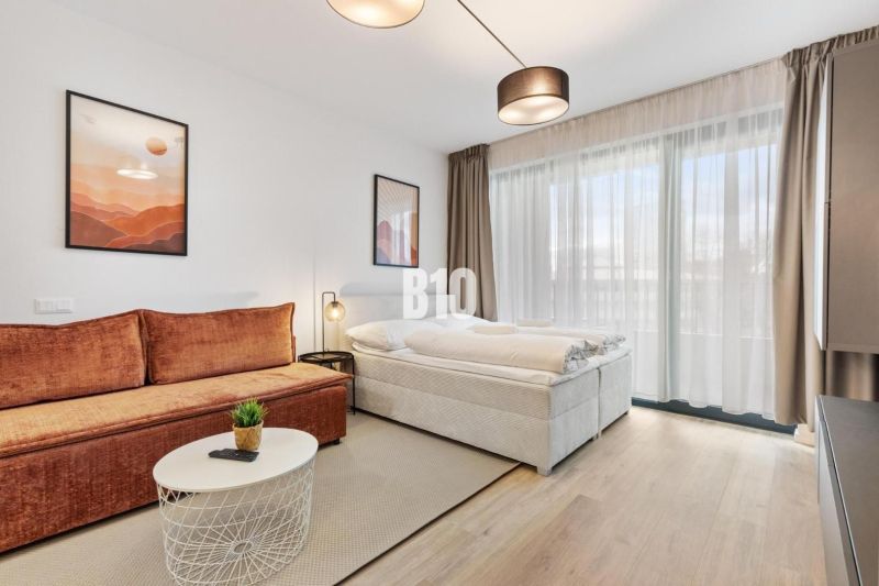 DOWNTOWN NA DOSAH – DIZAJNOVÝ 1-izbový apartmán s loggiou a výhľadom n - Obývacia časť 1-izbového bytu s pohovkou, posteľou a podlahou s dreveným dekorom.