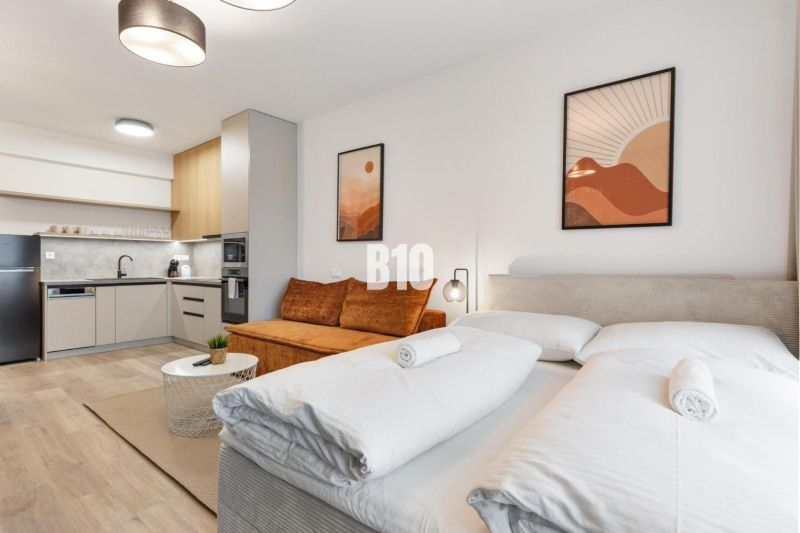 DOWNTOWN NA DOSAH – DIZAJNOVÝ 1-izbový apartmán s loggiou a výhľadom n - Interiér 1-izbového bytu s podlahou s dreveným dekorom, kuchyňa a posteľ.