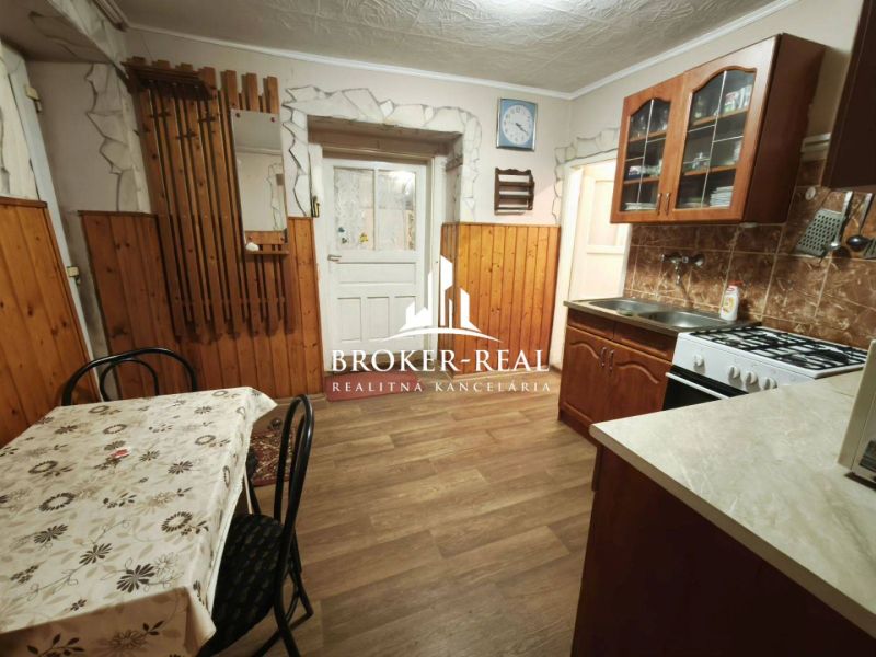 Rodinný dom 4 - izbový, Bódvaszilas, Maďarsko - Kuchyňa v rodinnom dome s podlahou s dreveným dekorom, jedálenským stolom a kuchynskou linkou.