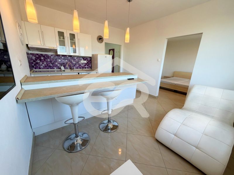 Na predaj kompletne prerobený 1 izbový byt, Vráble - Lúky, 36m2, 7/7 - Kuchyňa s barovým pultom v 1-izbovom byte, biely nábytok, fialový obklad a kreslo.