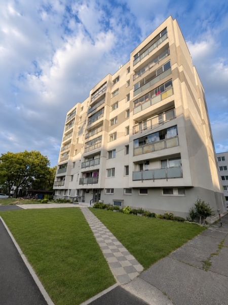 TOP Veľký rodinný 3-izbový byt s vlastným kúrením, loggiou a parkovaní - Bytový dom na Nobelovej ulici v Bratislave s upraveným trávnikom pred budovou.