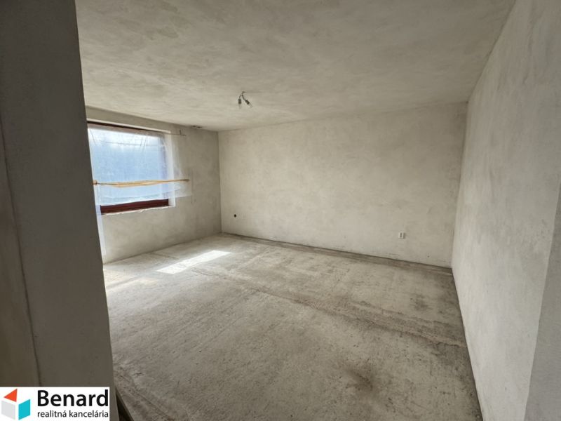 Rozostavaný rodinný dom Plavnica - Prázdna miestnosť v rodinnom dome s oknom, betónovou podlahou a bielymi stenami.