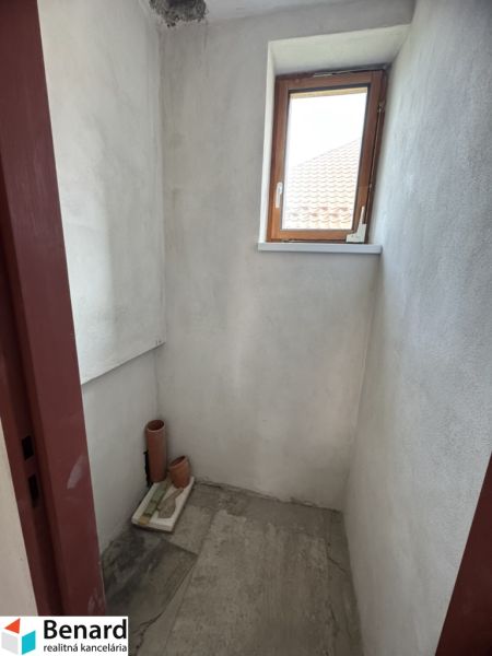 Rozostavaný rodinný dom Plavnica - Malá miestnosť s oknom v rodinnom dome, nefarbené steny, dlažba na podlahe.