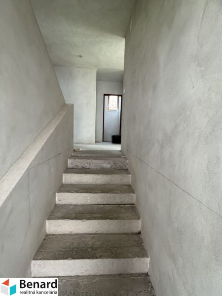 Rozostavaný rodinný dom Plavnica - Betónové schody vedúce na poschodie v rodinnom dome s omietnutými stenami.