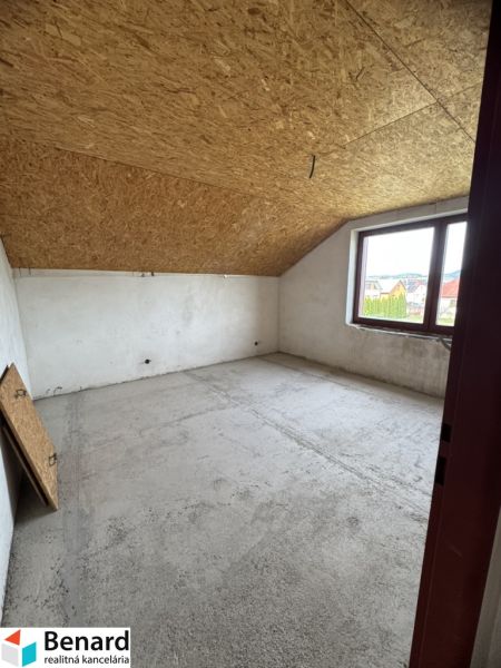 Rozostavaný rodinný dom Plavnica - Podkrovná izba v rodinnom dome s dreveným stropom a veľkým oknom.