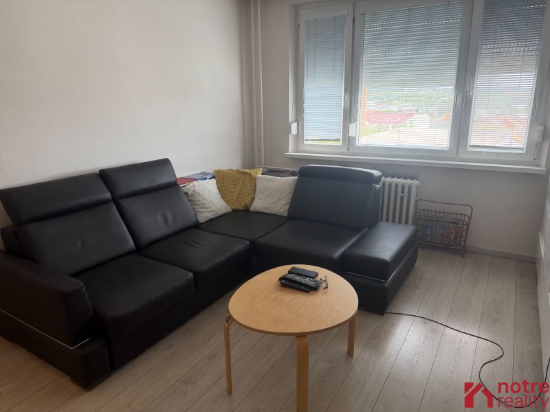 2,5 izbový byt v centre Lučenca - Obývacia izba v 2-izbovom byte s čiernym gaučom a podlahou s dreveným dekorom.