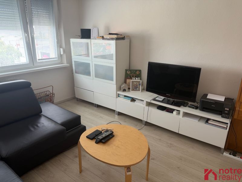 2,5 izbový byt v centre Lučenca - Obývacia izba v 2-izbovom byte s podlahou s dreveným dekorom a moderným nábytkom.