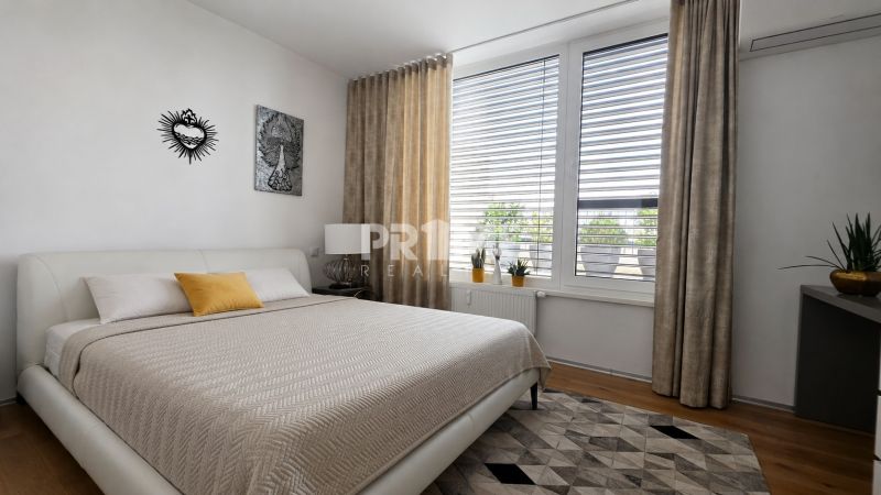 PENTHOUSE – moderný 2i byt s výnimočnou 69 m² terasou, AHOJ PARK - Spálňa v 2-izbovom byte s veľkým oknom, posteľou a dekoračnou podlahou s dreveným dekorom.