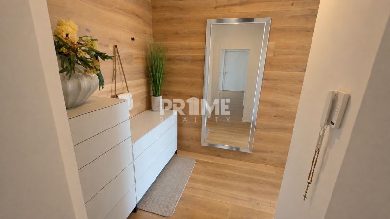 PENTHOUSE – moderný 2i byt s výnimočnou 69 m² terasou, AHOJ PARK - Interiér 2-izbového bytu s bielou komodou, zrkadlom a podlahou s dreveným dekorom.
