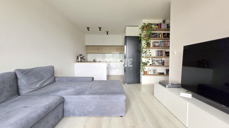 MODERNÝ 3i BYT, NOVOSTAVBA ČEREŠNE, LOGGIA, KLÍMA, PARKING, Polianky - Obývacia izba s pohovkou a TV, otvorenou kuchyňou a podlahou s dreveným dekorom.
