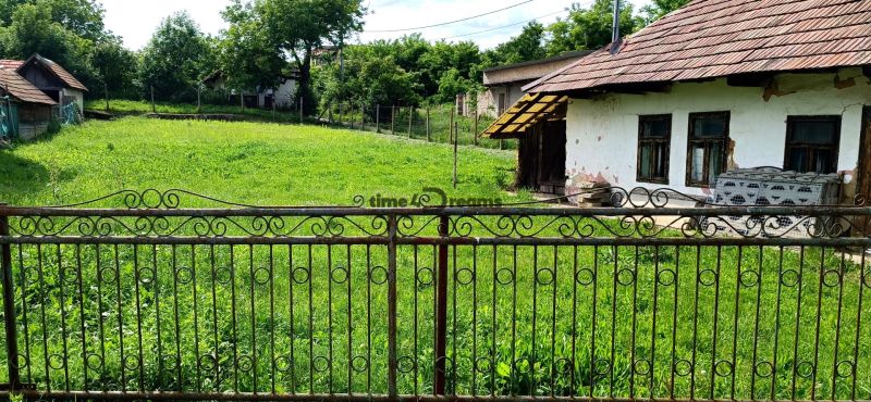 NA PREDAJ stavebný pozemok  v Plavých Vozokanoch - Starší dom s plotom na pozemku, obklopený zeleňou, ideálny pre bývanie.