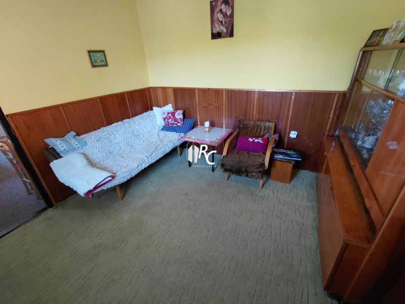 Rodinný dom Martin – Podháj, 5 izieb a pozemok 621 m² - Izba v rodinnom dome s pohovkou, kreslom a vitrínou, steny obložené drevom.