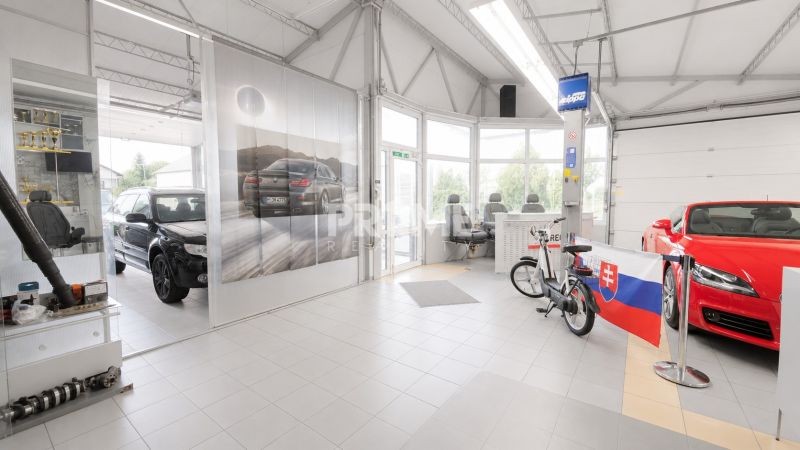 MODERNÝ, ZABEHNUTÝ, KOMPLETNE ZARIADENÝ AUTOSERVIS, LOZORNO - Výrobné priestory s vystavenými automobilmi, bicyklom a slovenskou vlajkou.