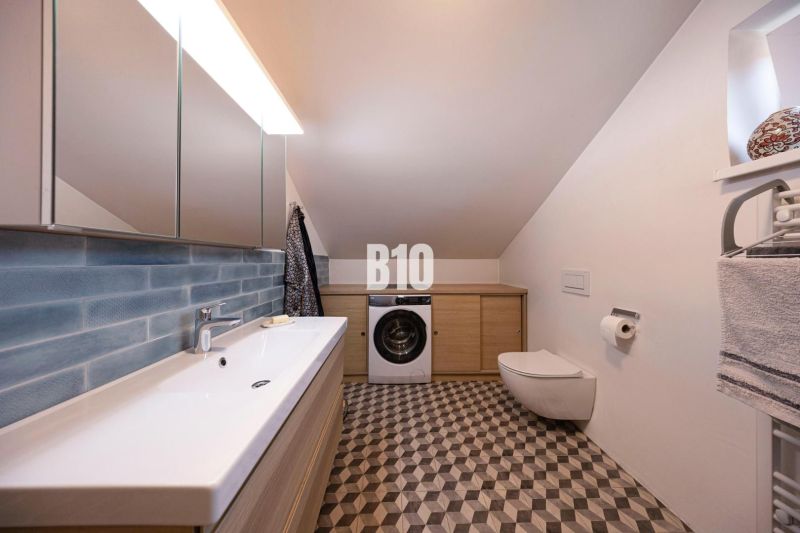 Priestranný 5-izbový rodinný dom (190 m²) s krásne upraveným 13a pozem - Kúpeľňa v rodinnom dome s práčkou, zrkadlom a umývadlom, geometrická dlažba.
