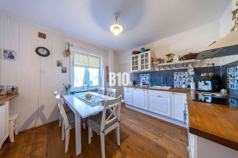 Priestranný 5-izbový rodinný dom (190 m²) s krásne upraveným 13a pozem - Kuchyňa v rodinnom dome s bielym nábytkom a podlahou s dreveným dekorom.
