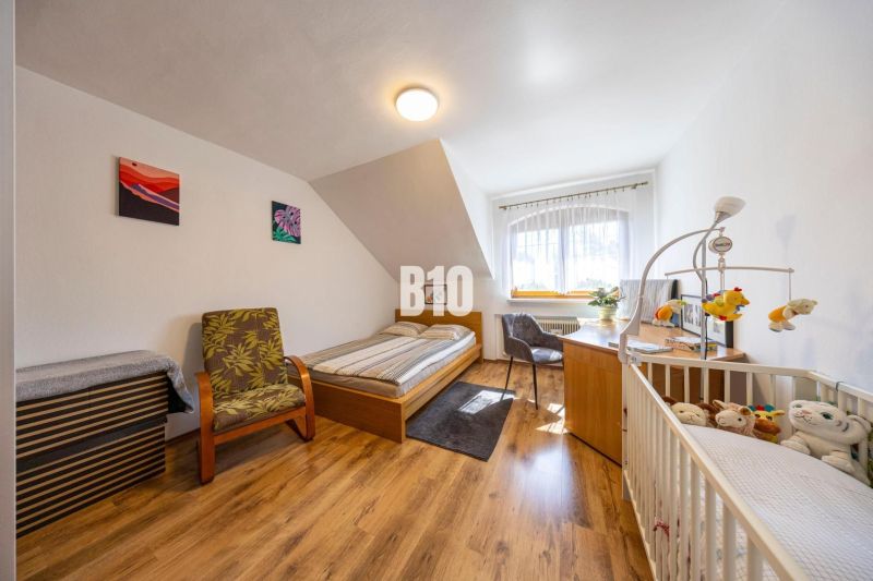 Priestranný 5-izbový rodinný dom (190 m²) s krásne upraveným 13a pozem - Spálňa v rodinnom dome s posteľou, detskou postieľkou a podlahou s dreveným dekorom.