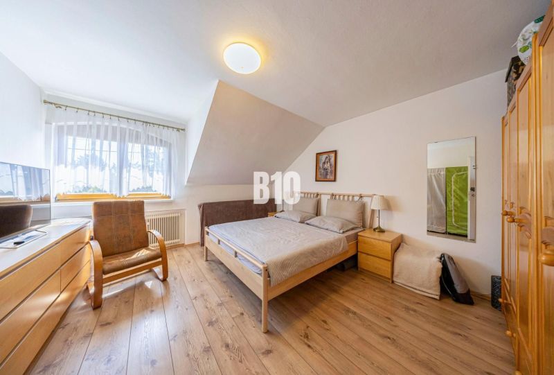 Priestranný 5-izbový rodinný dom (190 m²) s krásne upraveným 13a pozem - Spálňa v rodinnom dome s podlahou s dreveným dekorom, posteľou a kreslom.