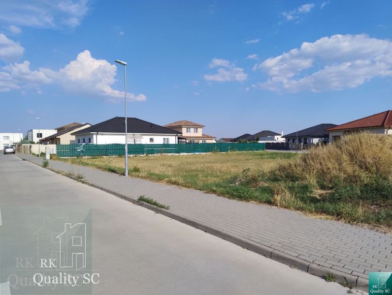 SENEC - NA PREDAJ exkluzívny stavebný pozemok pre rodinné domy - JUŽNÁ - Pozemky na bývanie v Senci obklopené domami a zeleňou pod modrou oblohou.