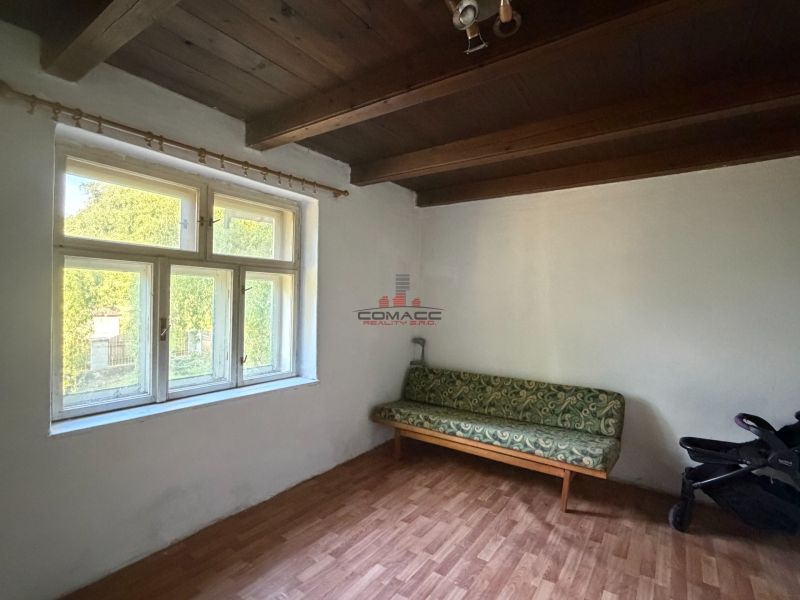 Exkl. 3 izbový rodinný dom v H. Orešanoch ZĽAVA - Izba v rodinnom dome s oknom, sedačkou, podlahou s dreveným dekorom a kočíkom.