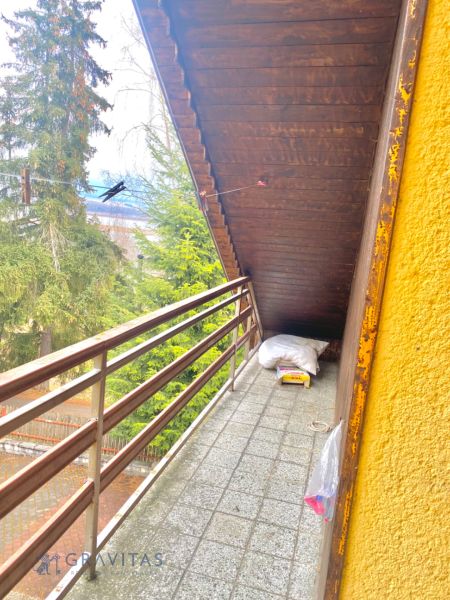 Rekreačný RD pri Oravskej Priehrade na Slanickej Osade - Balkón vily so strešnými doskami, výhľad na ihličnaté stromy a udržiavaný dvor.