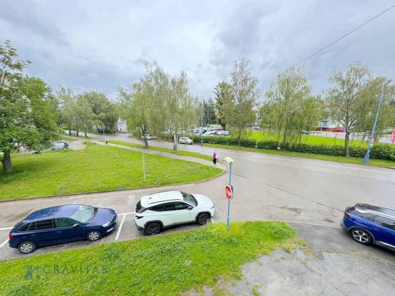 Na predaj 1-izbový byt Bratislavská ul., Dubnica Nad Váhom - Bratislavská ulica v Dubnici nad Váhom s autami a zeleňou pri 1-izbovom byte.