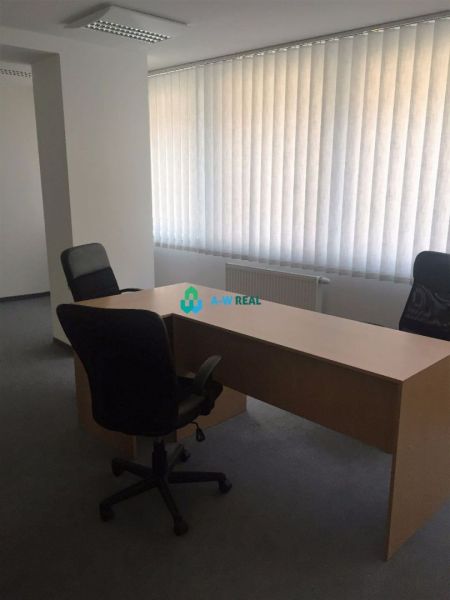 Kancelárie v centre mesta. - Jednoduchá kancelária s dreveným stolom, dvoma stoličkami a žalúziami na oknách.