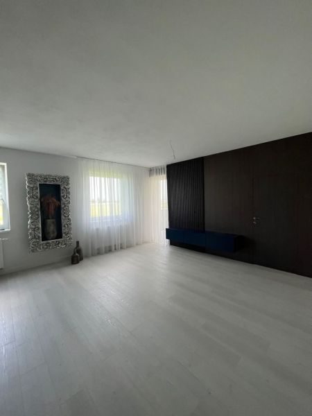 Luxusný byt na prenájom úplne nový kompletne zariadený s garážou. - Interiér priestrannej miestnosti s bielou podlahou a tmavými stenami v 3-izbovom byte.