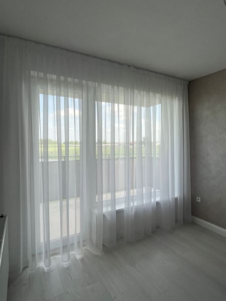 Luxusný byt na prenájom úplne nový kompletne zariadený s garážou. - Biela záclona v 3-izbovom byte, podlaha s dreveným dekorom a svetlá stena.