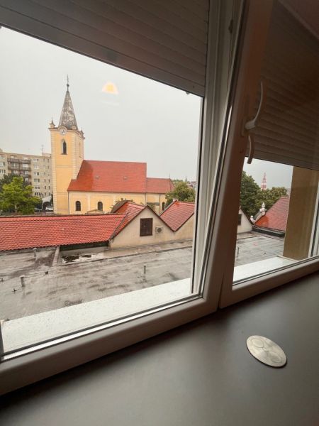 Voľný od 1 oktobra.Byt v centre mesta na prenájom - Výhľad z okna 1-izbového bytu na kostol v Dunajskej Strede počas zamračeného dňa.