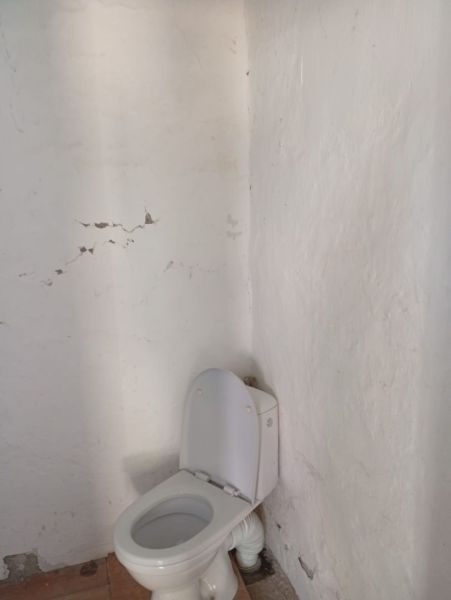 Vidiecky domček na predaj. - Kúpeľňa v rodinnom dome s bielou toaletou a popraskanou omietkou na stenách.