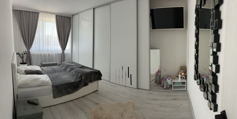 Ůžasný rodinný dom v obci Trstice. - Spálňa v rodinnom dome s podlahou s dreveným dekorom, záclony, zrkadlo a televízia.