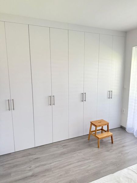 Luxusný byt na prenájom. - Biely vstavaný šatník s dreveným dekorom a stoličkou v 2-izbovom byte.