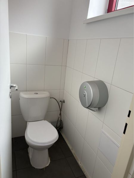 Prenájom nebytového priestoru na podnikateľské účely v CENTRE Dunajske - Toaleta v bielej dlažbe s oknom a držiakom na toaletný papier.
