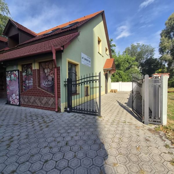Na prenájom polyfunkčný objekt v DS - Budova v Dunajskej Strede s bránou, zelenou fasádou a reklamnými plochami.