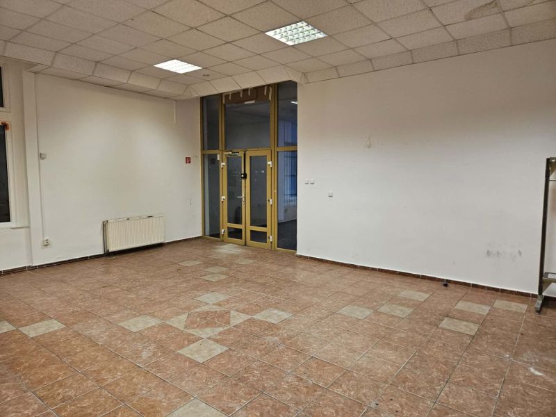 Exkluzívny obchodný priestor na prenájom v centre Dunajskej Stredy – u - Prázdny obchodný priestor s podlahou z dlaždíc, biele steny a veľké okná.