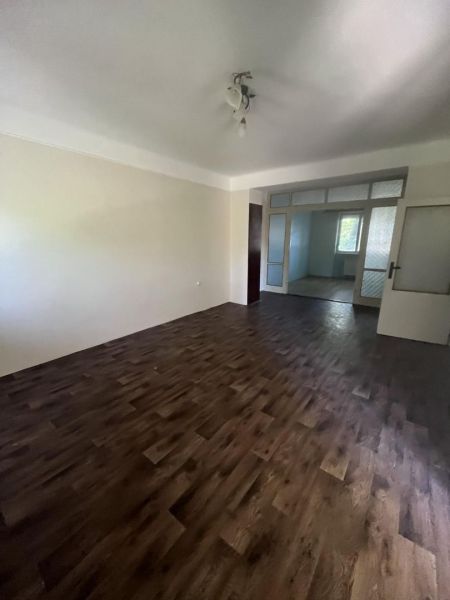 Nová ponuka – 3 izbový byt na predaj v Dunajskej Strede - Priestranná izba v 3-izbovom byte s podlahou s dreveným dekorom a vstupom do ďalšej miestnosti.