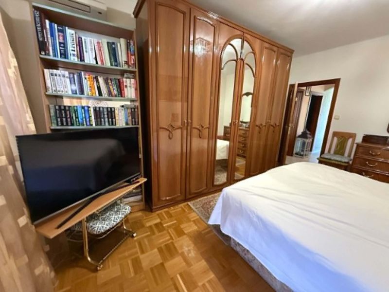 Klasika, ktorá sa neodmieta - Spálňa v 3-izbovom byte s knihovnicou, televízorom, zrkadlovou skriňou a podlahou s dreveným dekorom.