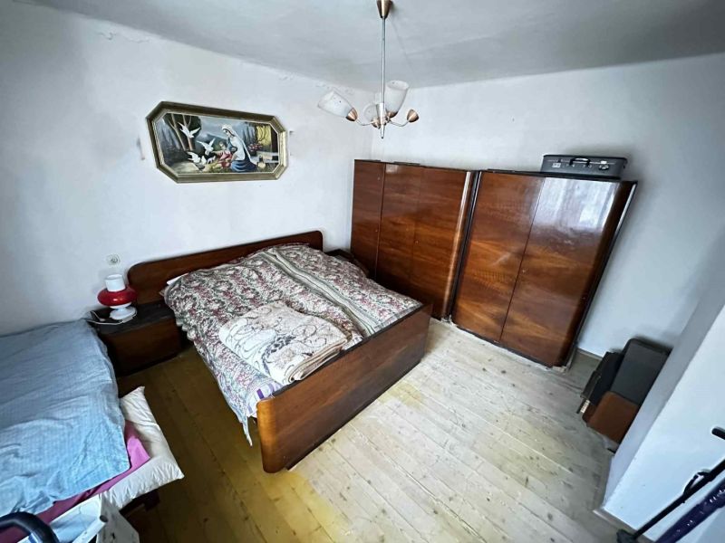 Na predaj starší rodinný dom vhodný na kompletnú prestavbu s  veľkým p - Spálňa v rodinnom dome s drevenou skriňou, obrazom nad posteľou a podlahou s dreveným dekorom.