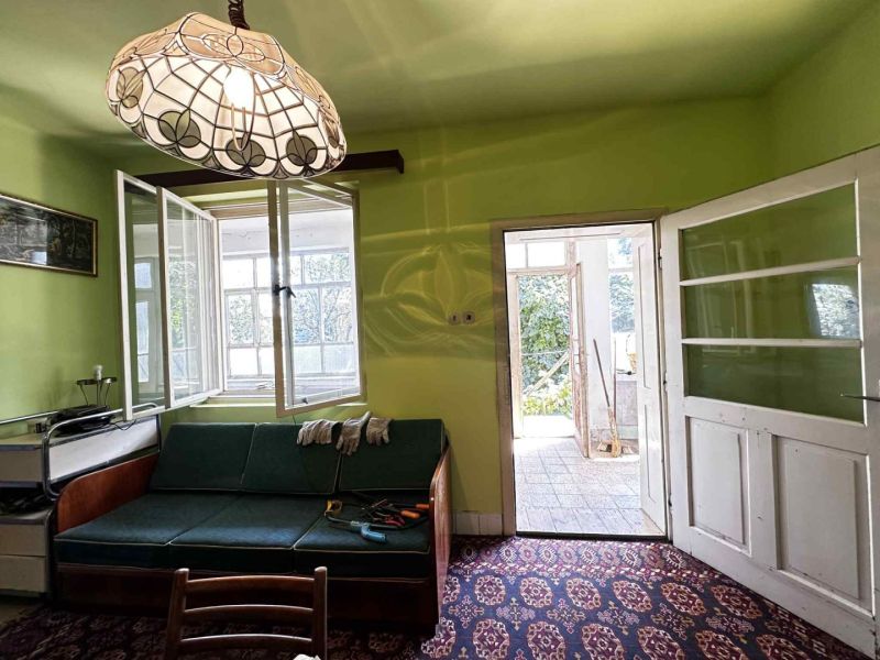 Na predaj starší rodinný dom vhodný na kompletnú prestavbu s  veľkým p - Svetlo zelená stena, sedacia súprava, vintage lampa a otvorené dvere v rodinnom dome.