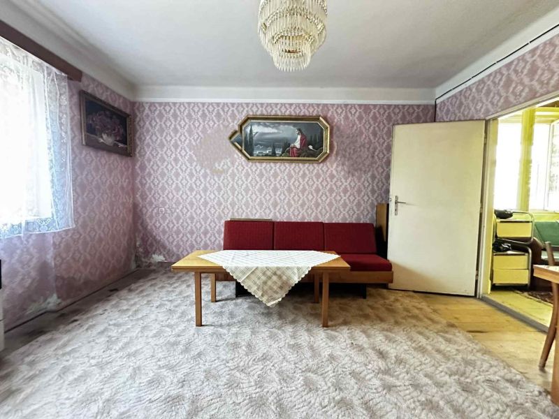 Na predaj starší rodinný dom vhodný na kompletnú prestavbu s  veľkým p - Obývacia izba v rodinnom dome s červenou sedačkou a dekoratívnymi tapetami.