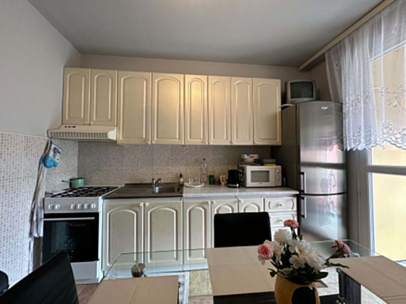 Na predaj kompletne zariadený 3 izbový byt s klimatizáciou aj s balkón - Kuchyňa v 3-izbovom byte s krémovými skrinkami, spotrebičmi a prestretým stolom.