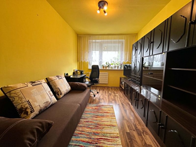 Na predaj kompletne zariadený 3 izbový byt s klimatizáciou aj s balkón - Izba v 3-izbovom byte s hnedou sedačkou a podlahou s dreveným dekorom.