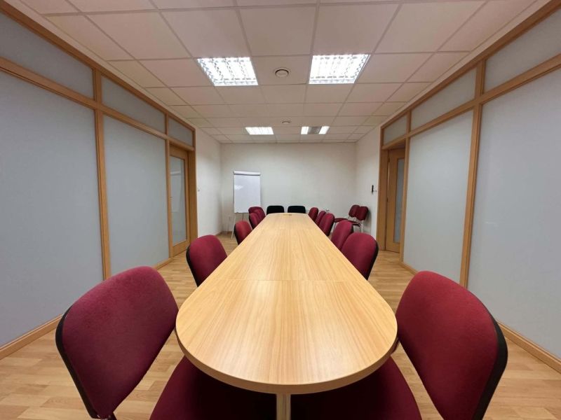 Na prenájom menšia  kancelária v centre mesta DS - 12,94 m2 - Konferenčná miestnosť v kanceláriách s dlhou drevenou stolom a podlahou s dreveným dekorom.